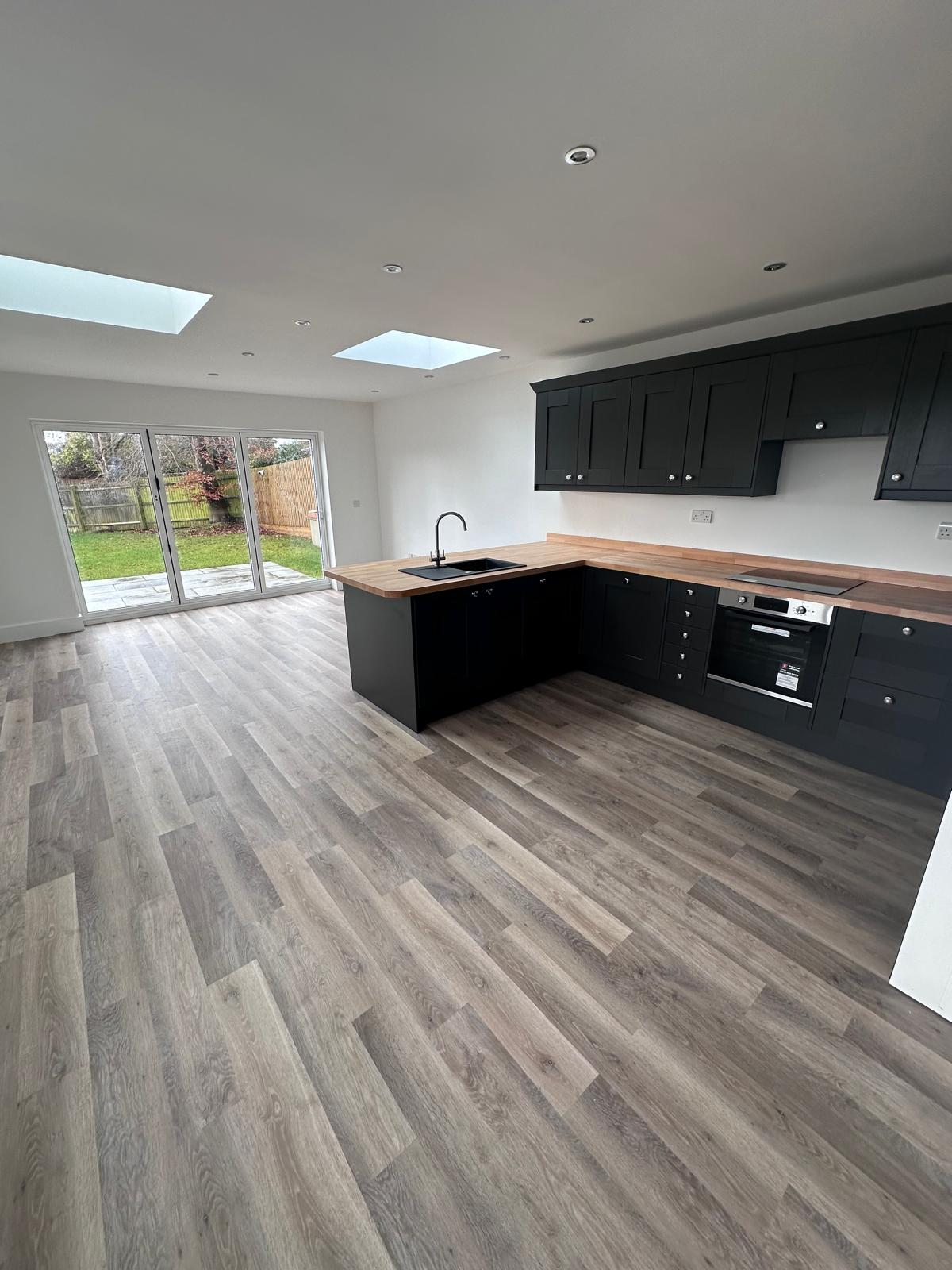 Open plan kitchen extension with dark shaker units, oak worktops, roof lights and bi-fold doors by DBD Builders Ltd