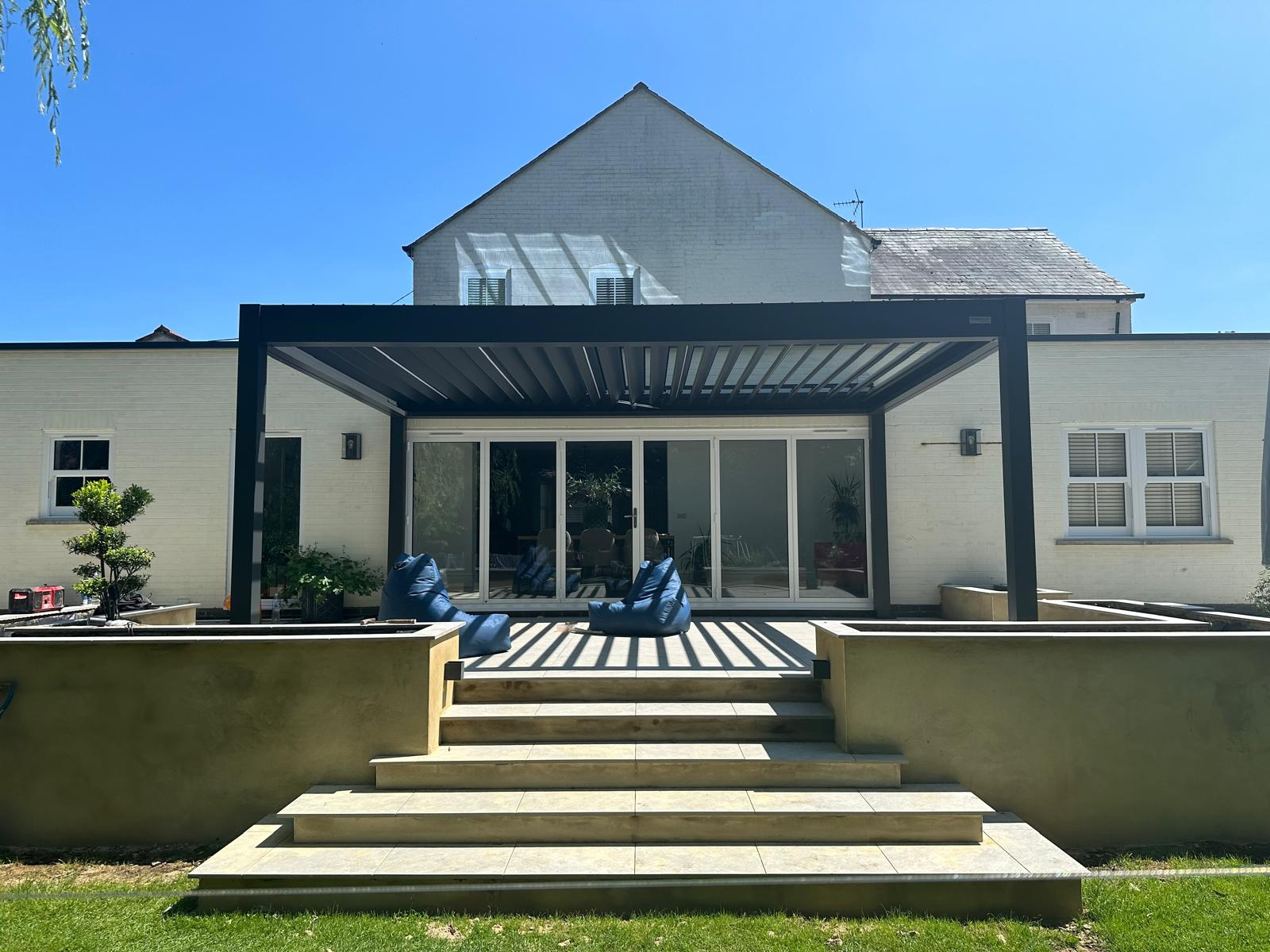 Rear extension with bi-fold doors and louvred aluminium pergola over a raised patio by DBD Builders Ltd
