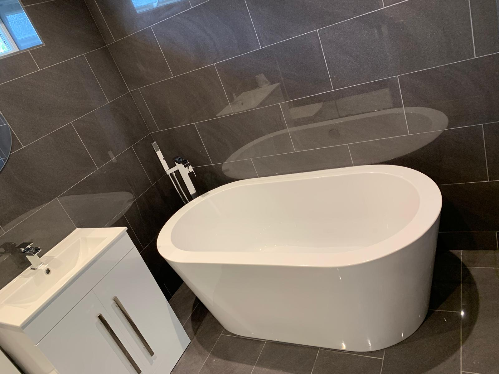 Fitted bathroom with freestanding oval bath, chrome floor-standing tap and dark grey large format tiling by DBD Builders Ltd